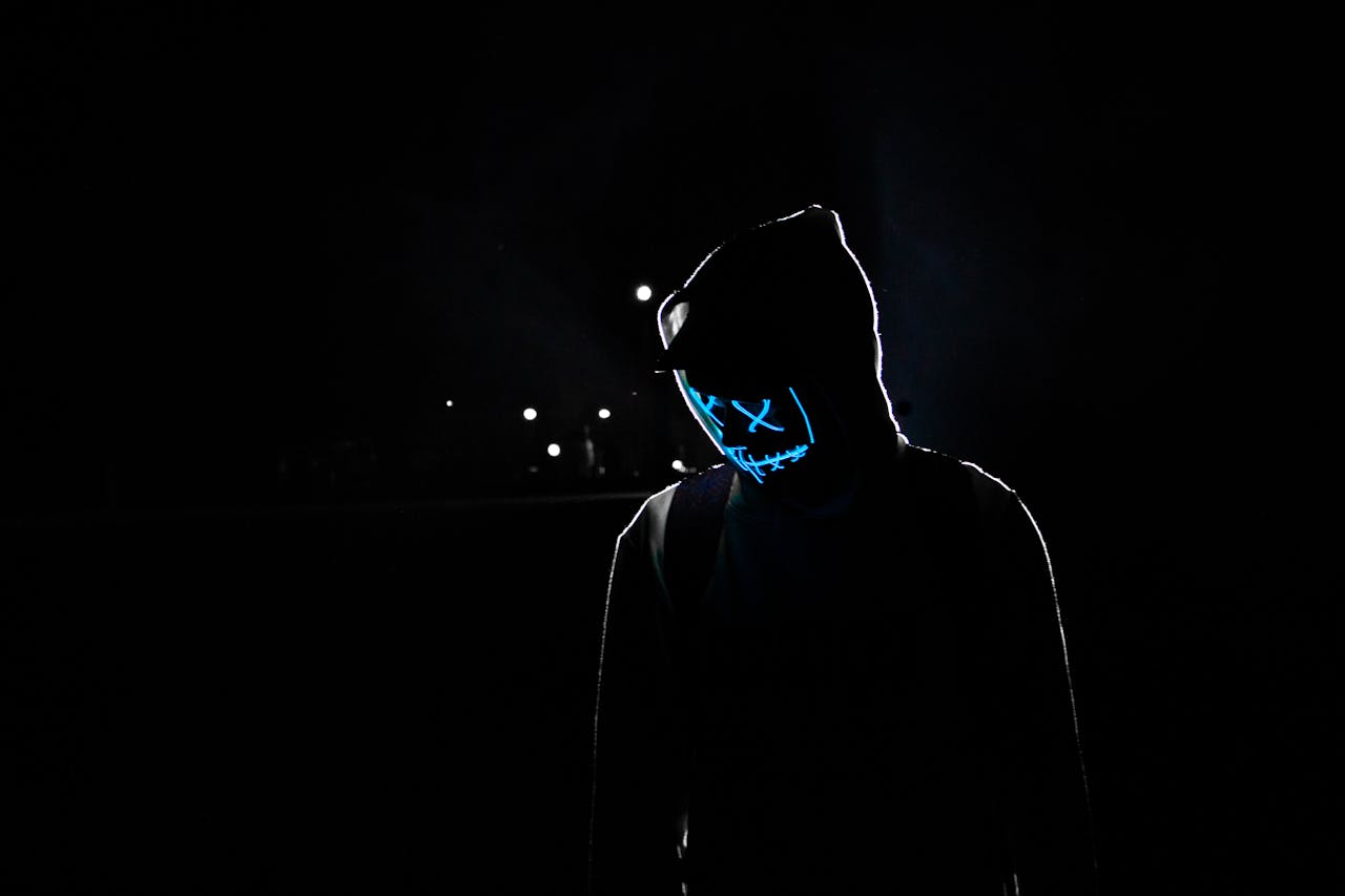 hero-img-01 Silhouette of a person in a hoodie wearing a glowing LED mask against a dark background.